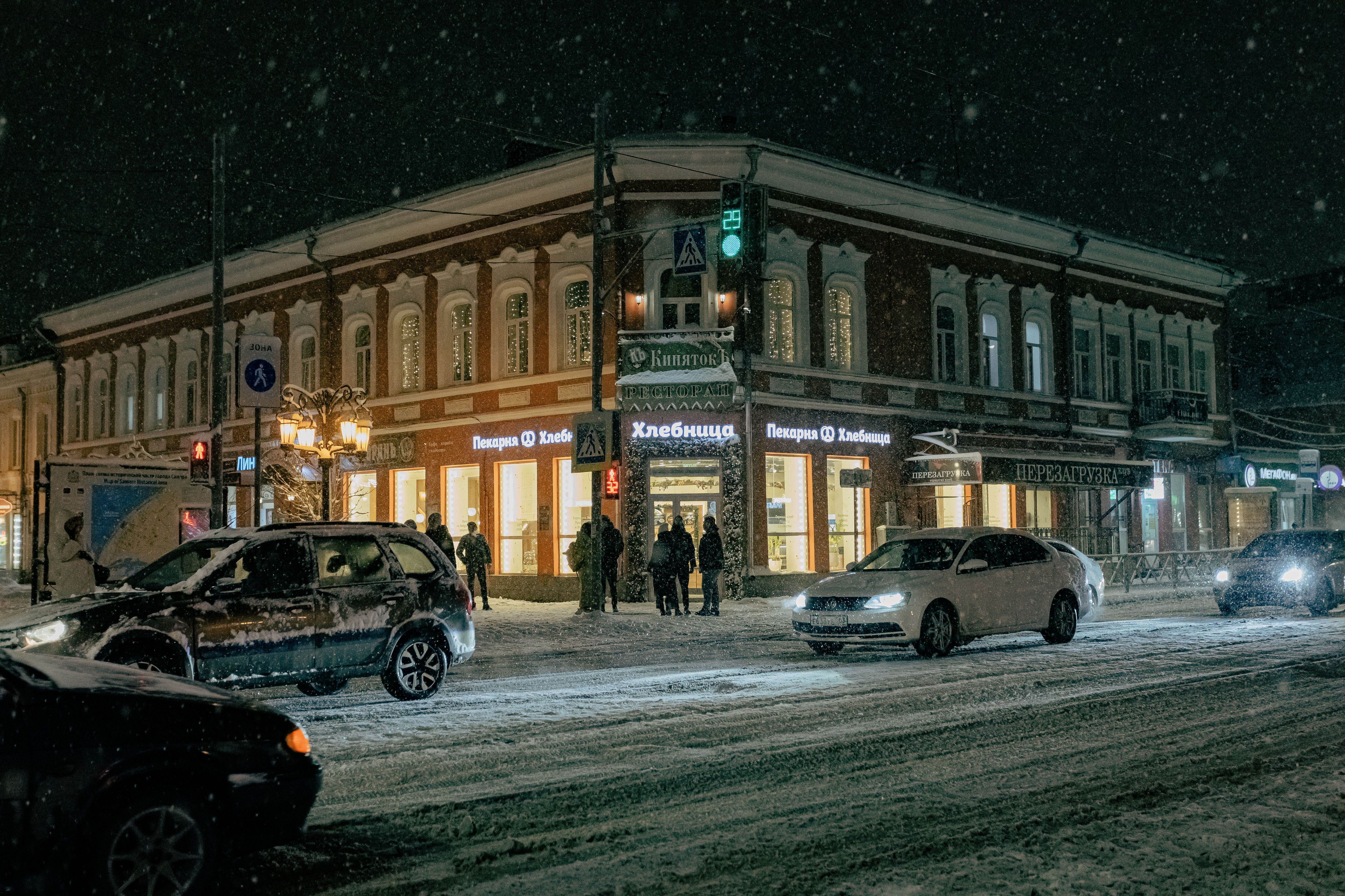 Cozy winter street scene at night with snowfall in a city intersection.