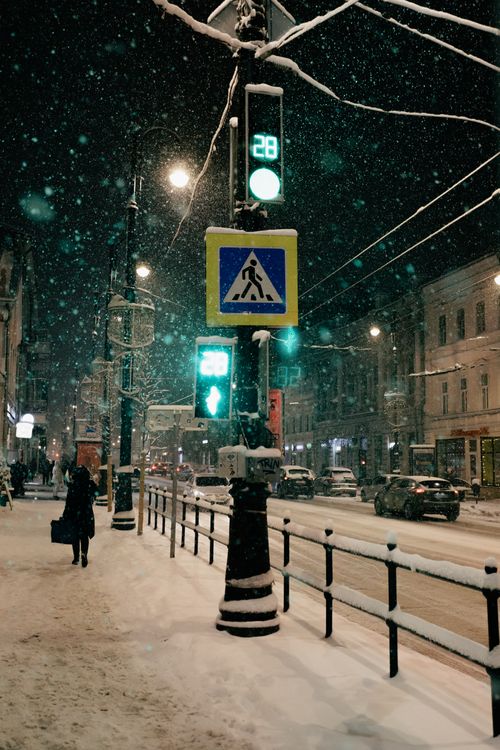 Free Urban night scene with snowfall, pedestrian crossing, and cars. Captivating winter cityscape. Stock Photo
