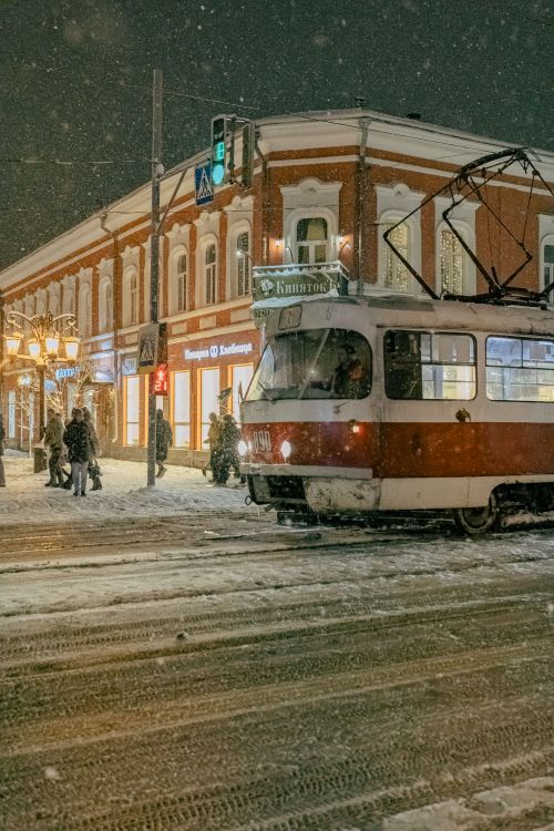 Free A red tram moves through a snowy city street at night, creating a vintage urban scene. Stock Photo