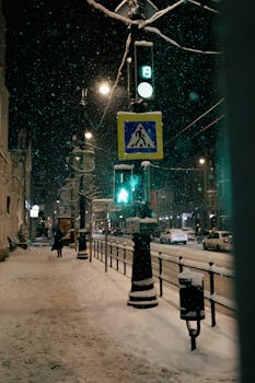 A snowy city street at night with traffic lights and pedestrians.