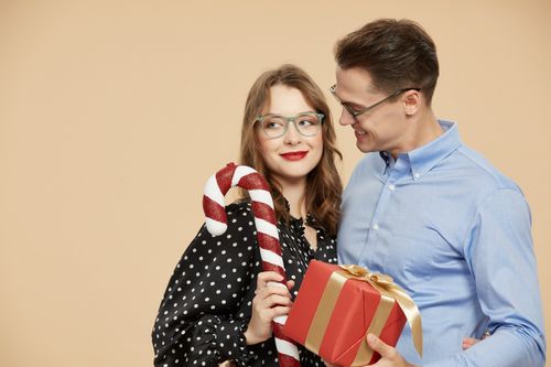 Free Smiling couple in eyeglasses embracing holiday joy with gifts and candy cane. Stock Photo
