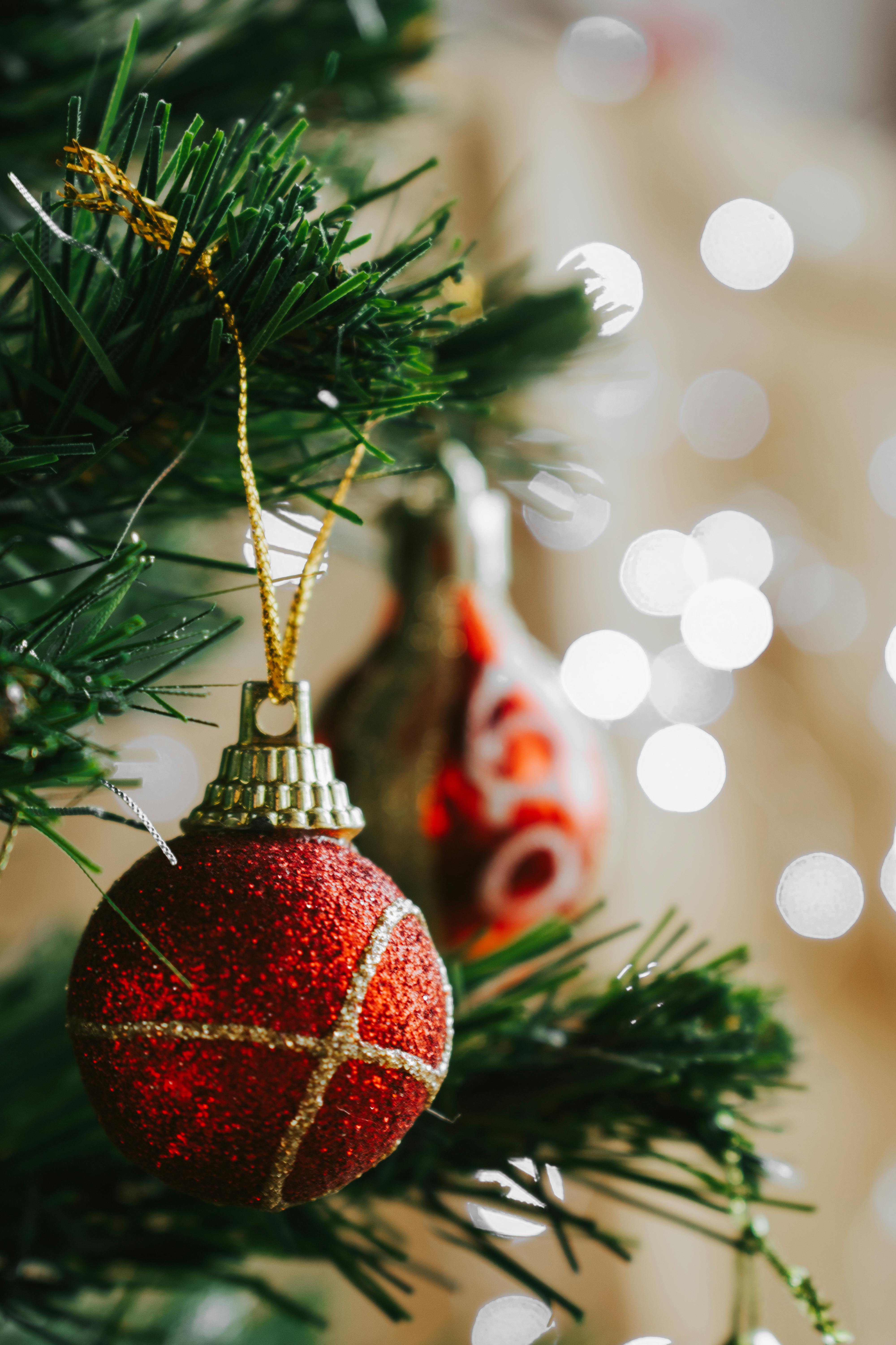Close-up of a red ornament hanging on a Christmas tree with festive bokeh lights in the background.