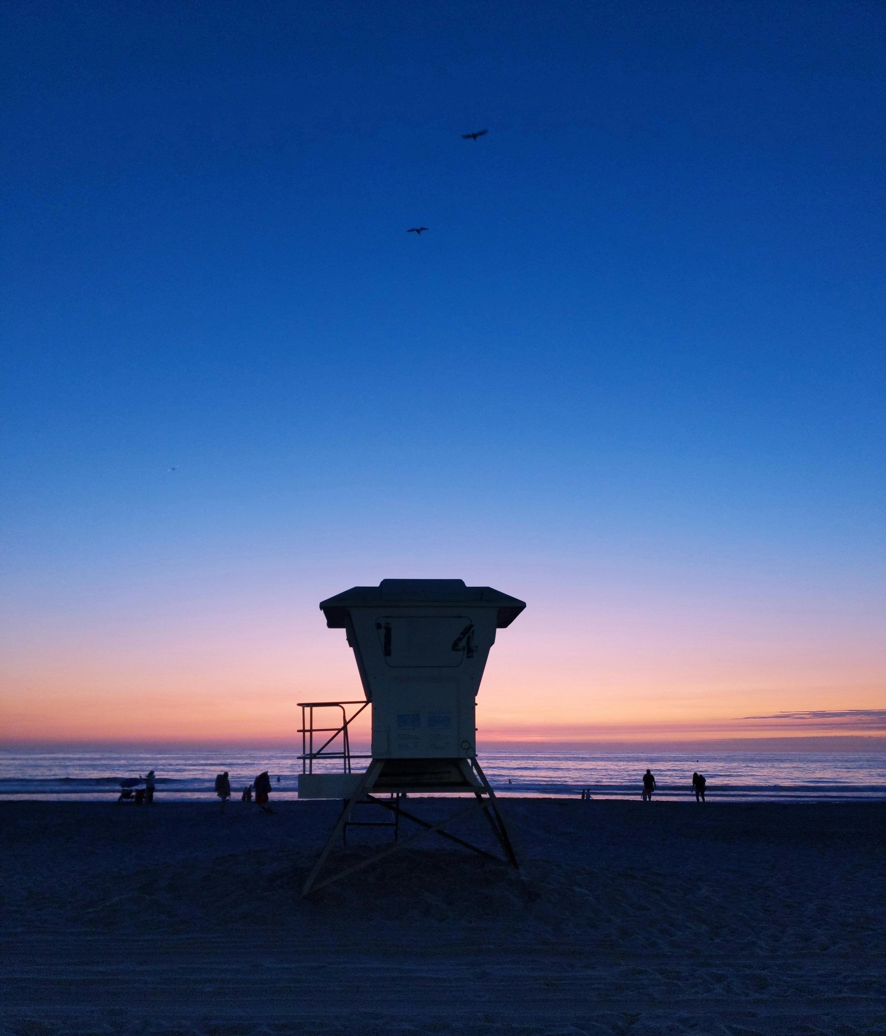 夕阳下，救生员塔的剪影与海滩上的人们共同构成了一幅生动的画面