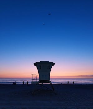 夕阳下，救生员塔的剪影与海滩上的人们共同构成了一幅生动的画面