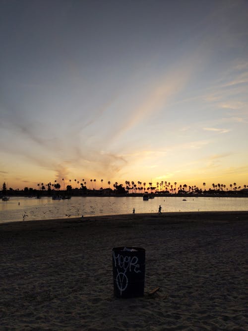 무료 파란색과 주황색 하늘 아래 해변에 흑인과 백인 쓰레기통 스톡 사진