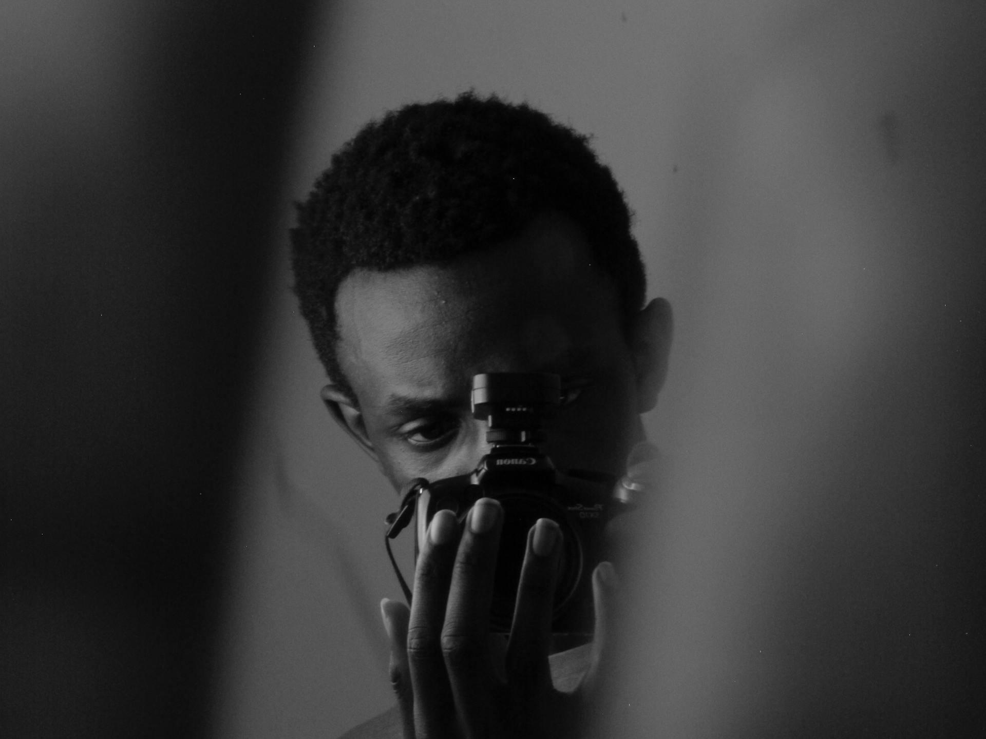 Dramatic black and white portrait of a photographer capturing a shot indoors.