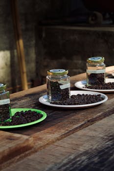 Coffee beans displayed in jars on rustic wooden table, highlighting texture and natural light.