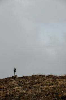 在法国梅泽尔的草地山顶上，一位孤独的徒步旅行者站在喜怒无常的多云天空下
