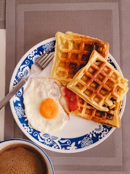 A mouth-watering breakfast of waffles, fried egg, and coffee on a decorative plate.