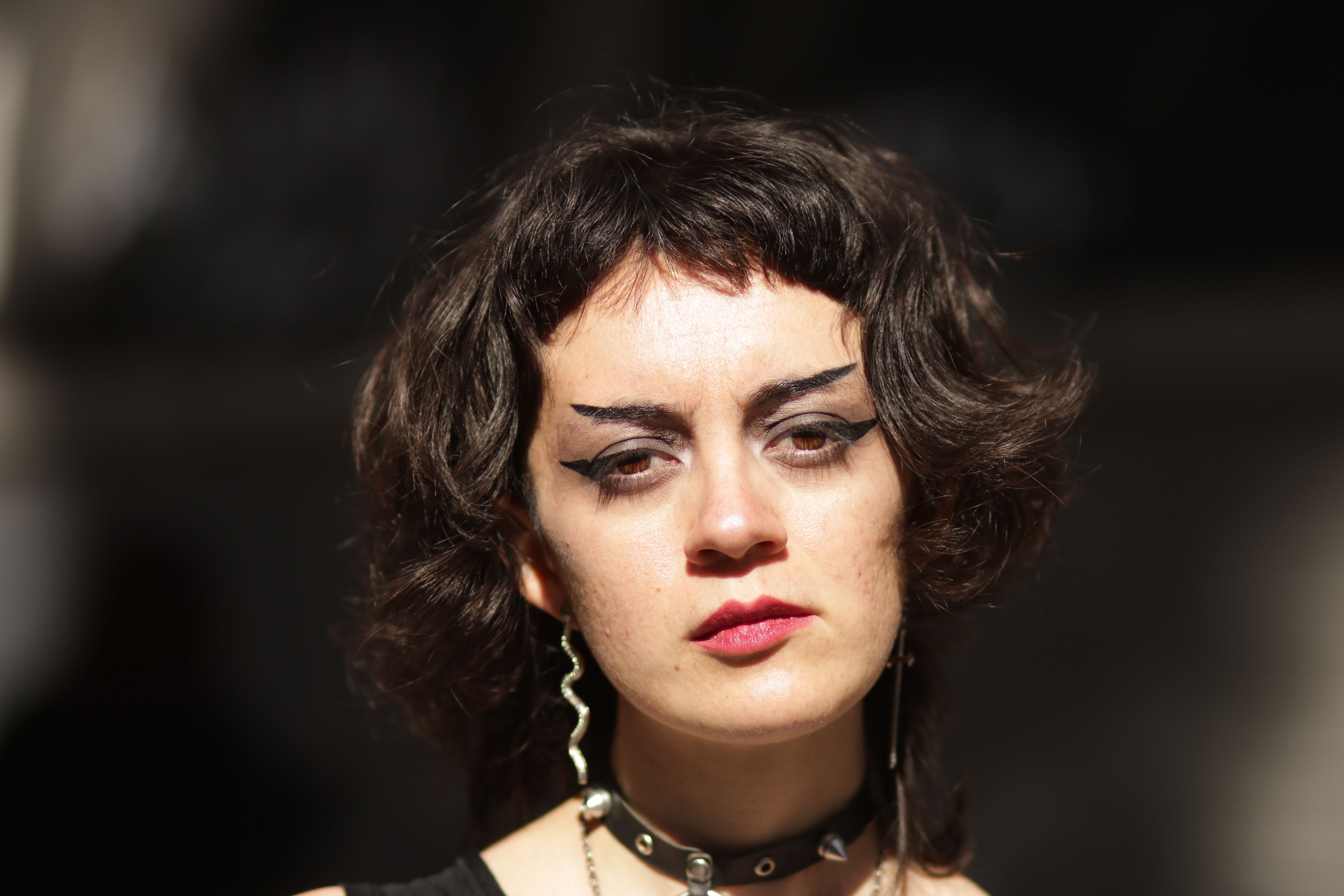Close-up portrait of a woman with bold eyeliner and short hair outdoors in sunlight.