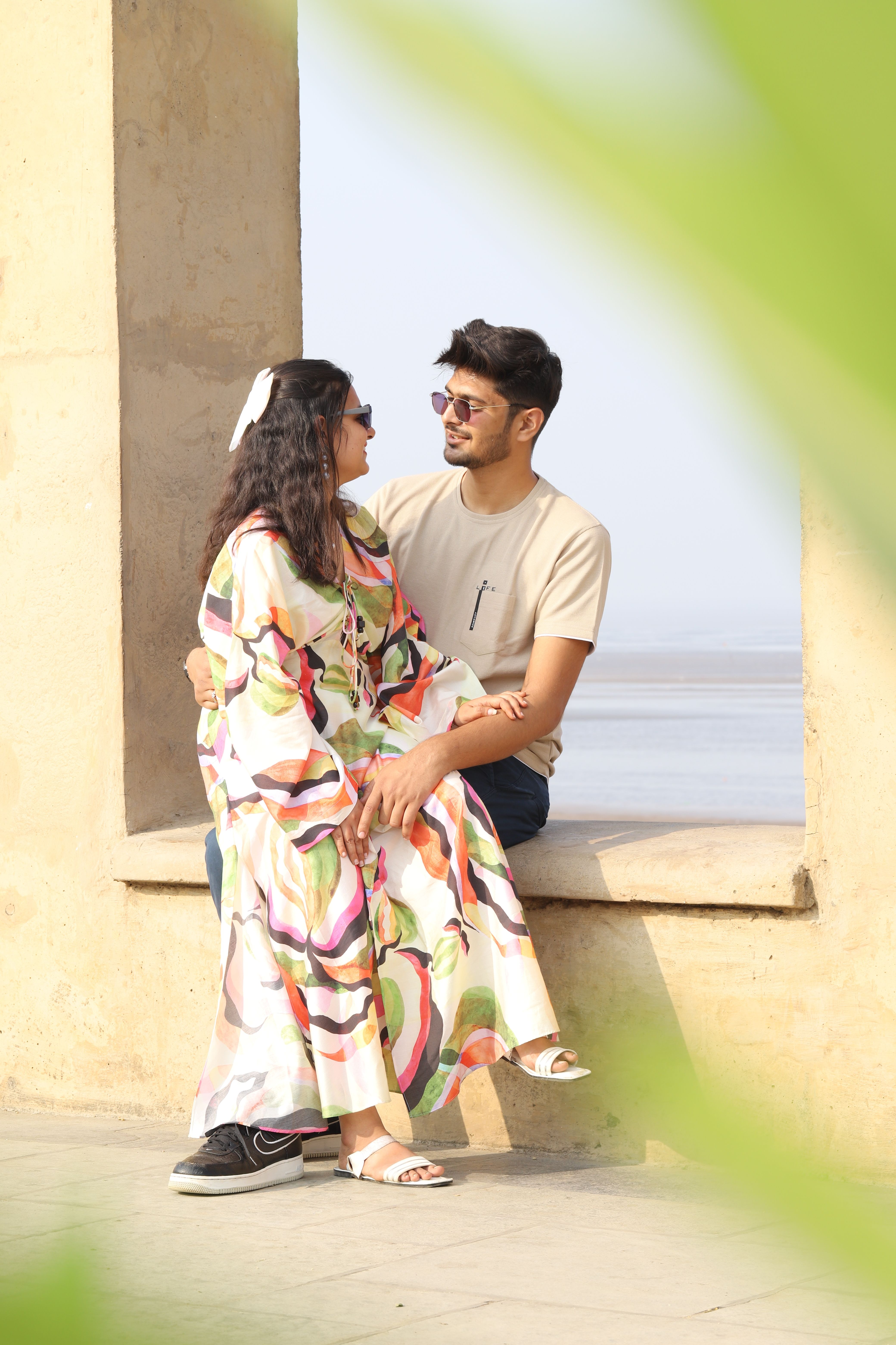 A couple in stylish outfits sitting by the beach, sharing a romantic moment.