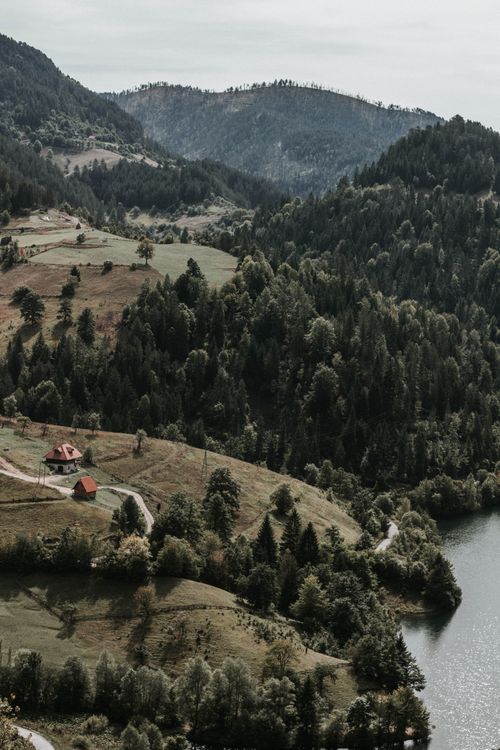 Free A tranquil aerial view of a lush forest and lake surrounded by mountains, showcasing nature's beauty. Stock Photo