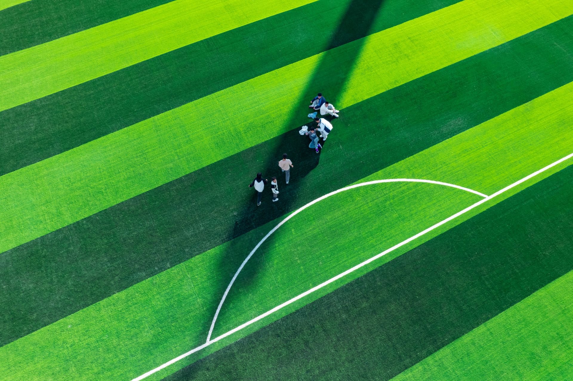Aerial perspective of a striped green soccer field with a group of people standing near the center line.