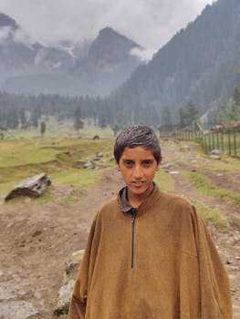 A young boy stands in a misty mountain landscape, showcasing natural beauty and serenity.