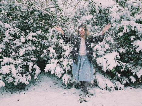 A woman enjoys a snowy day, surrounded by lush snow-covered trees in a winter garden.