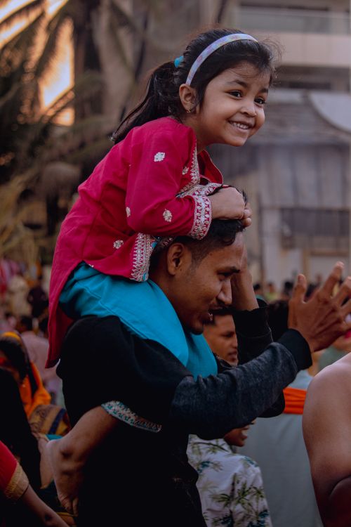 Free A joyful moment of a father carrying his smiling daughter on his shoulders during a festive event in Mumbai. Stock Photo