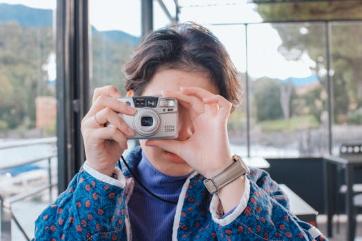 A person photographing outdoors with a vintage camera, showcasing a stylish outfit and scenic background.