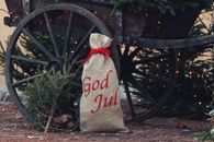 Rustic Christmas scene featuring a 'God Jul' sack by an old wooden cart in Jönköping, Sweden.