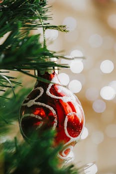 Close-up of a red Christmas ornament hanging on a tree with bokeh lights.