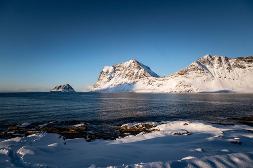 Free Breathtaking snowy mountains along a serene coastal shore, captured at sunset. Stock Photo