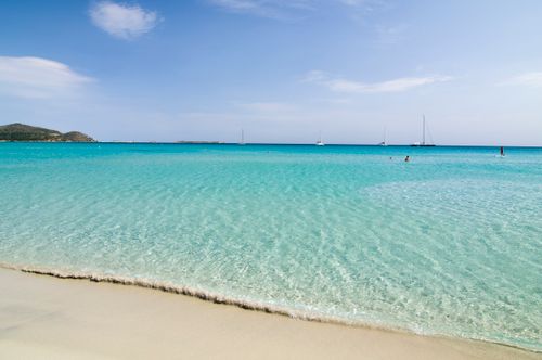 Free Tranquil beach scene with pristine turquoise waters and distant sailboats under a sunny sky. Stock Photo