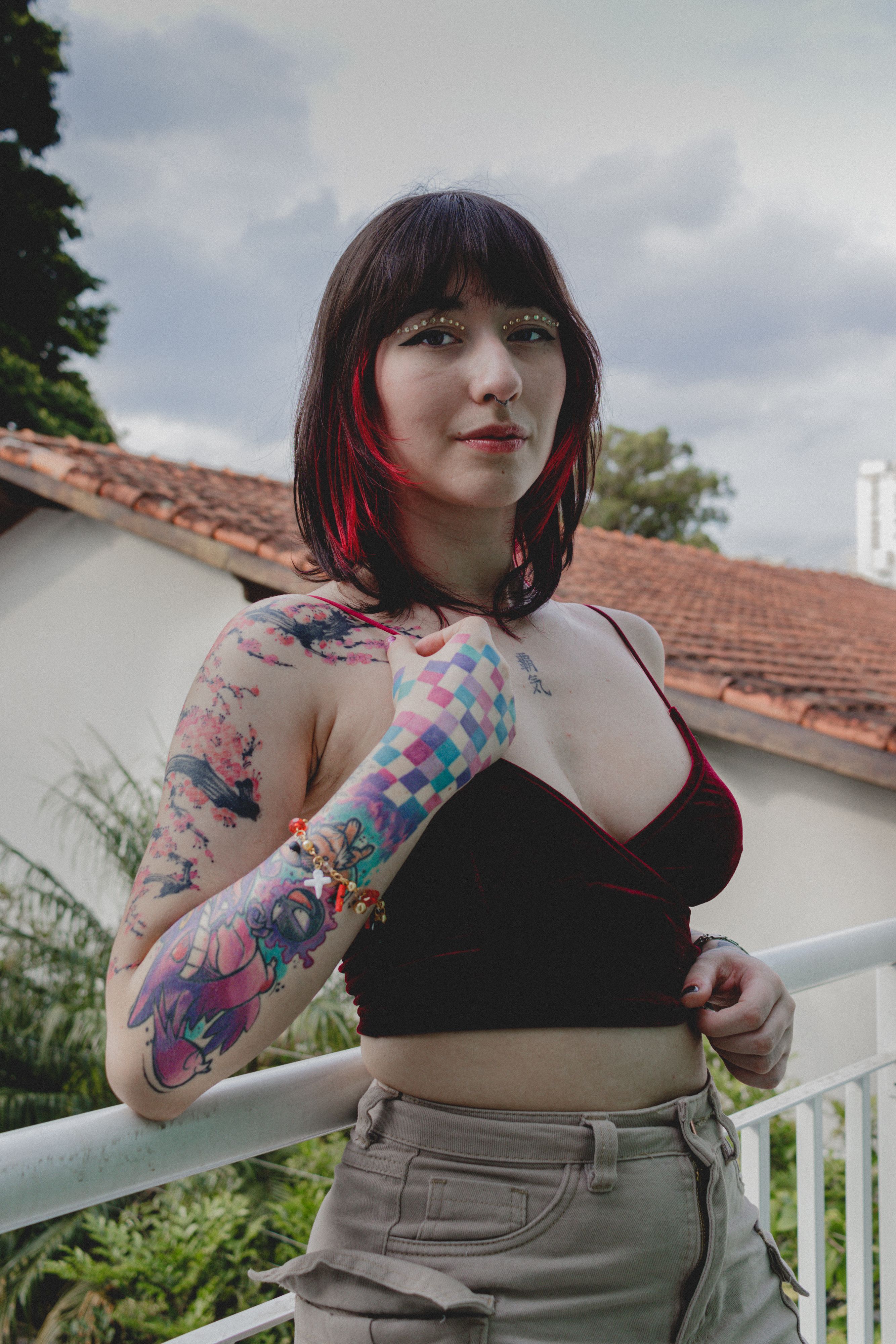 Portrait of a young woman with vibrant tattoos posing confidently outdoors, under a cloudy sky.