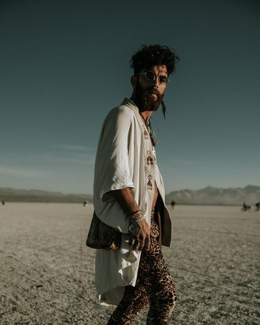 A stylish man poses in a desert landscape, showcasing a blend of vintage and modern fashion.