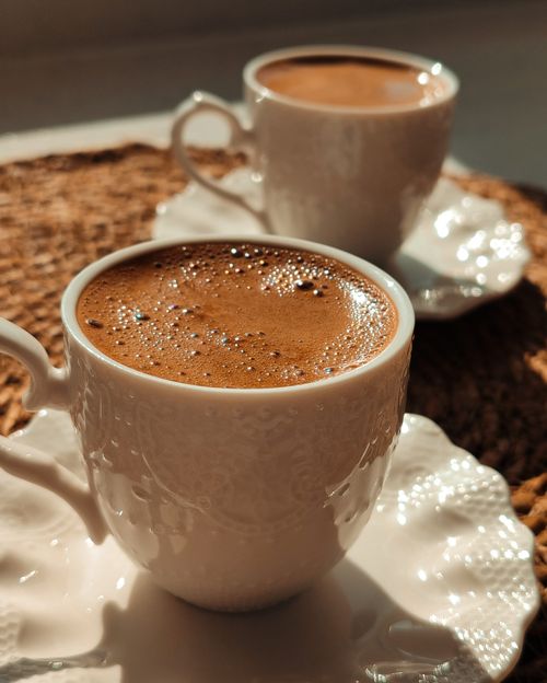 Free A close-up of two ceramic cups filled with traditional Turkish coffee on a woven mat. Stock Photo
