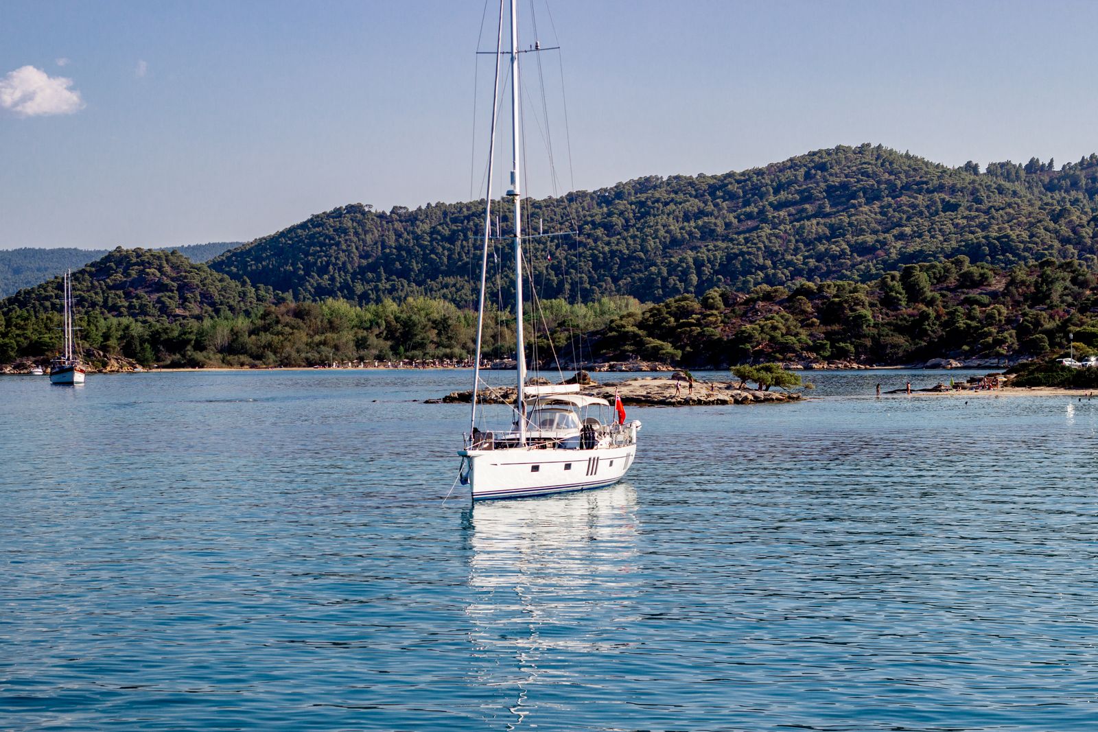Sailboat gliding on calm blue Mediterranean water with green hills in the background
