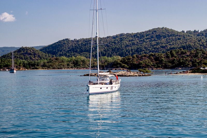 Sailboat gliding on calm blue Mediterranean water with green hills in the background