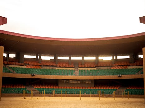 A vacant arena in Niger with colorful seating and a sandy floor, captured during the day.