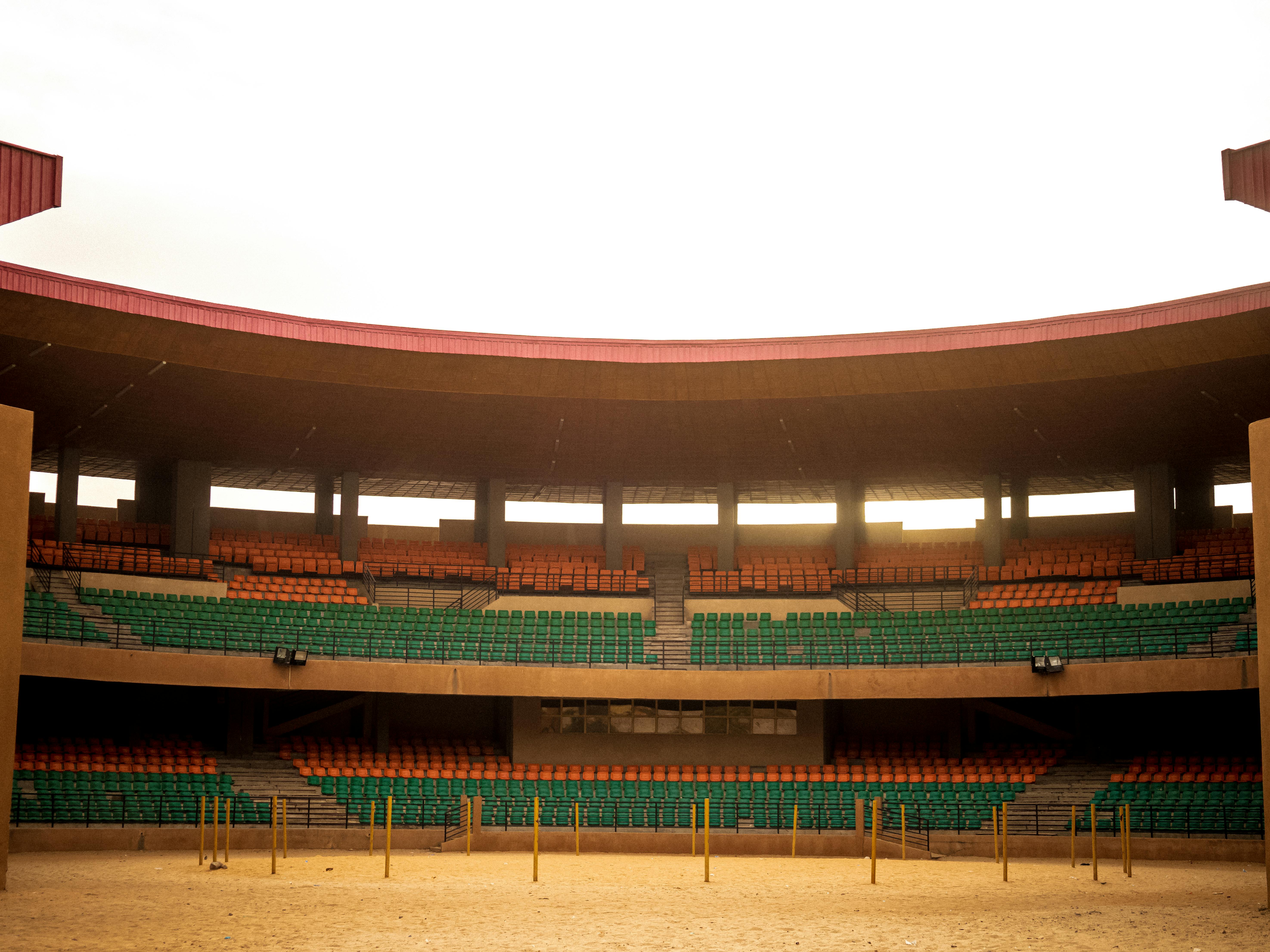 Kostenlos Eine leere Arena in Niger mit bunten Sitzgelegenheiten und Sandboden, aufgenommen bei Tageslicht. Stock-Foto