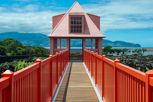 Free A vibrant red bridge leads to a picturesque house set in the scenic Azores landscape. Stock Photo