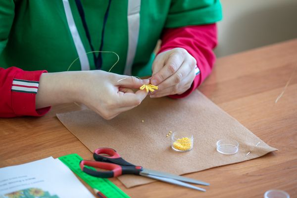 Hands threading small beads into a charm at a workbench — photo by Sergei Starostin on Pexels