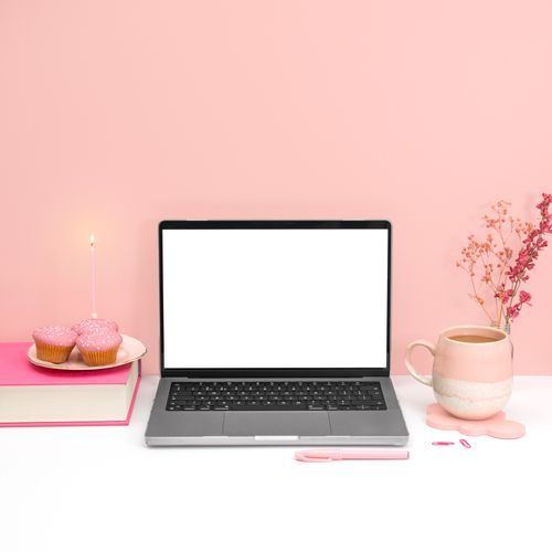 Free A pink aesthetic workspace featuring a laptop mockup, cupcakes, and a coffee mug for a creative office setup. Stock Photo
