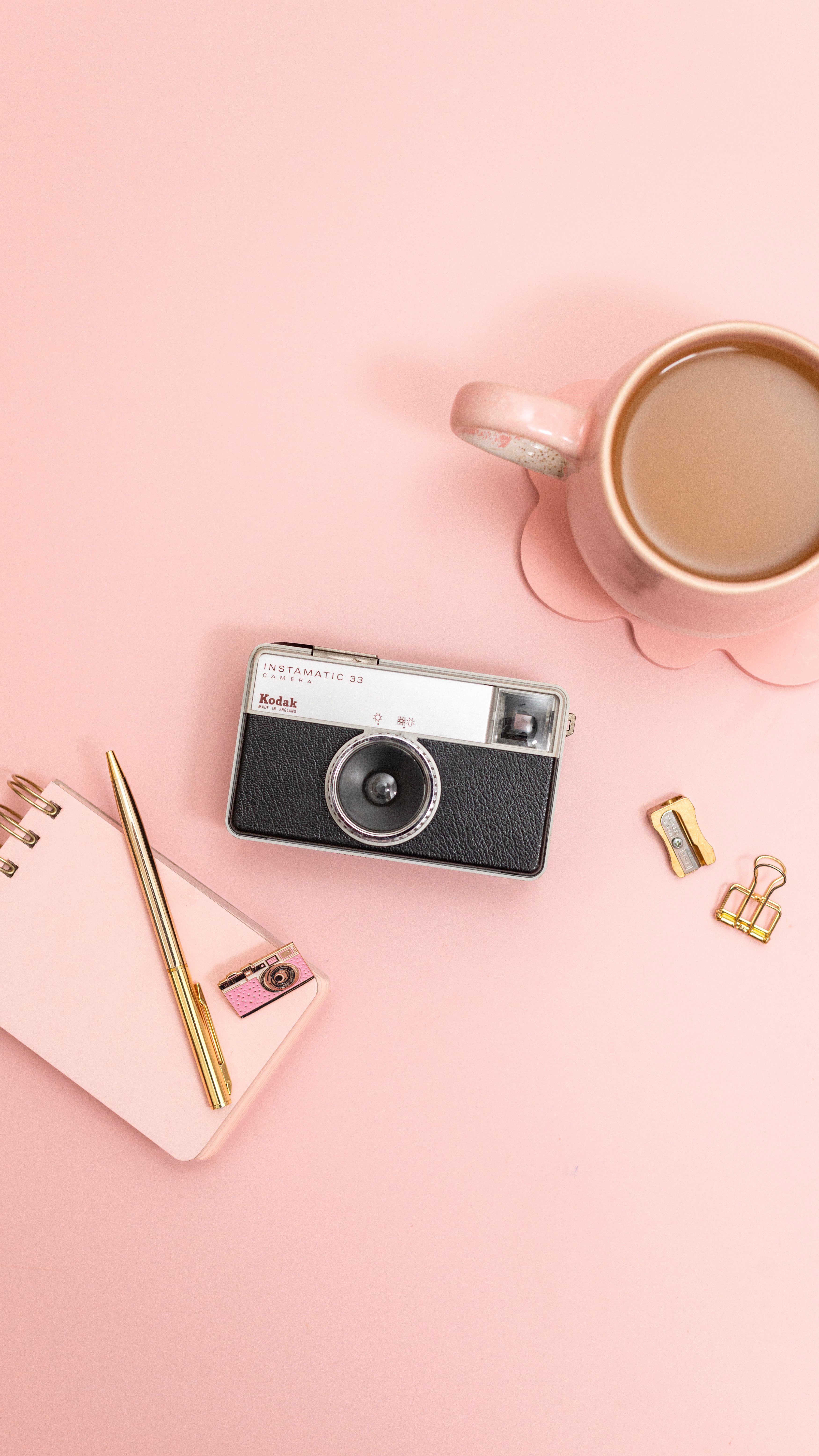 Kostnadsfria Snygg rosa skrivbordsplatta med vintagekamera, kaffemugg och brevpapper. Stock foto