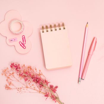 Flat lay of pink office supplies including a notebook, pen, and dried flowers on a desk.（イメージ）