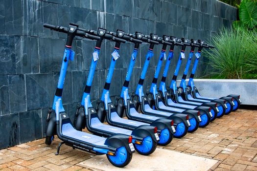 Bright blue electric scooters neatly lined up against a wall in Londrina, Brazil.
