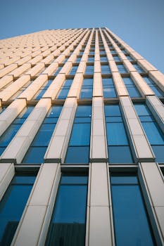 Upward view of a modern skyscraper with large reflective glass windows against a blue sky.