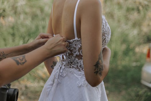 A bride dresses for her outdoor wedding ceremony, showcasing intricate embroidery.