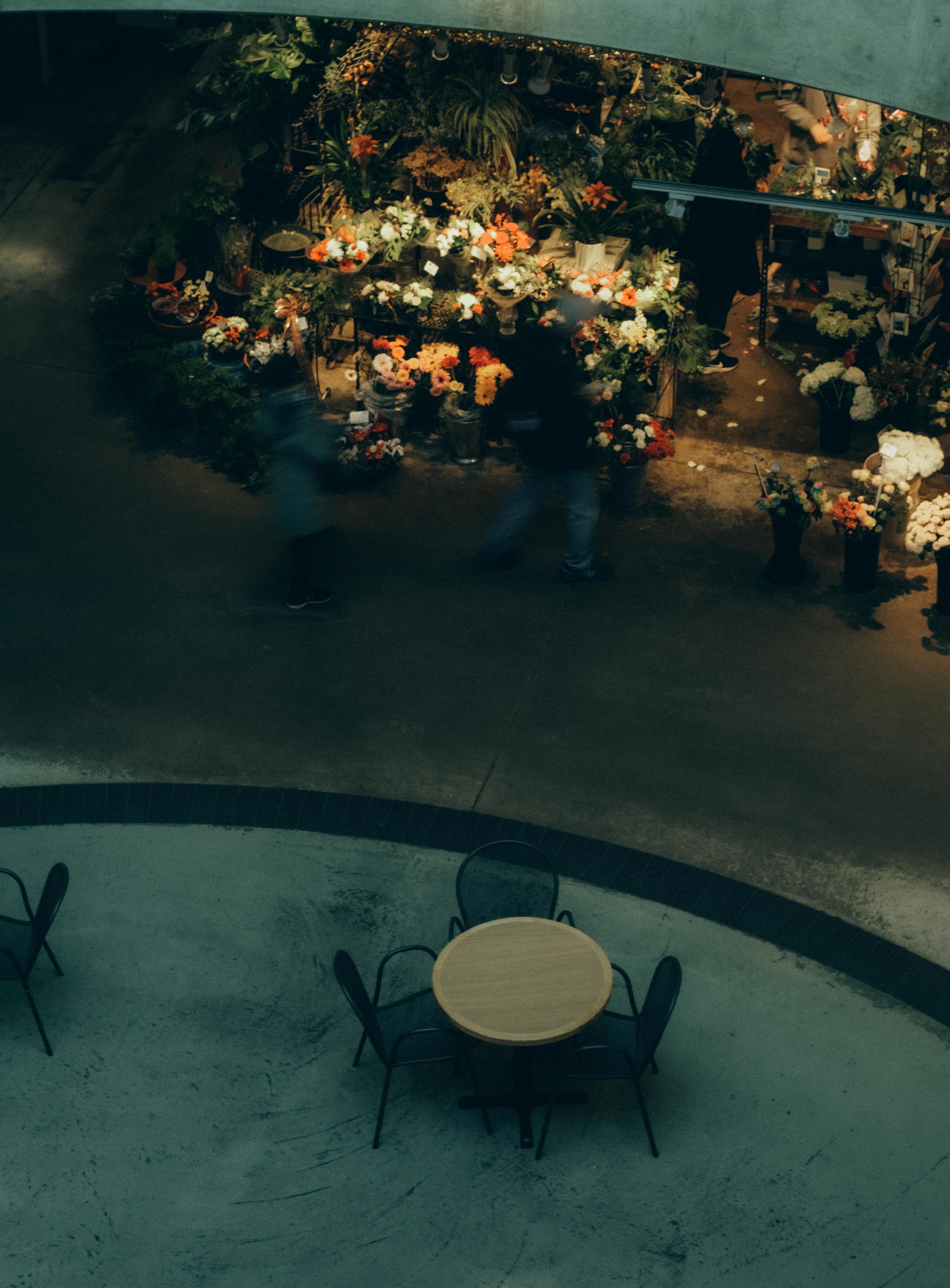 Atmospheric view of an indoor flower market, blurred motion of people, empty chairs and table.