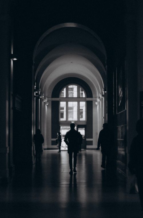 Free Moody black and white capture of a silhouette walking through an arched architectural hallway. Stock Photo