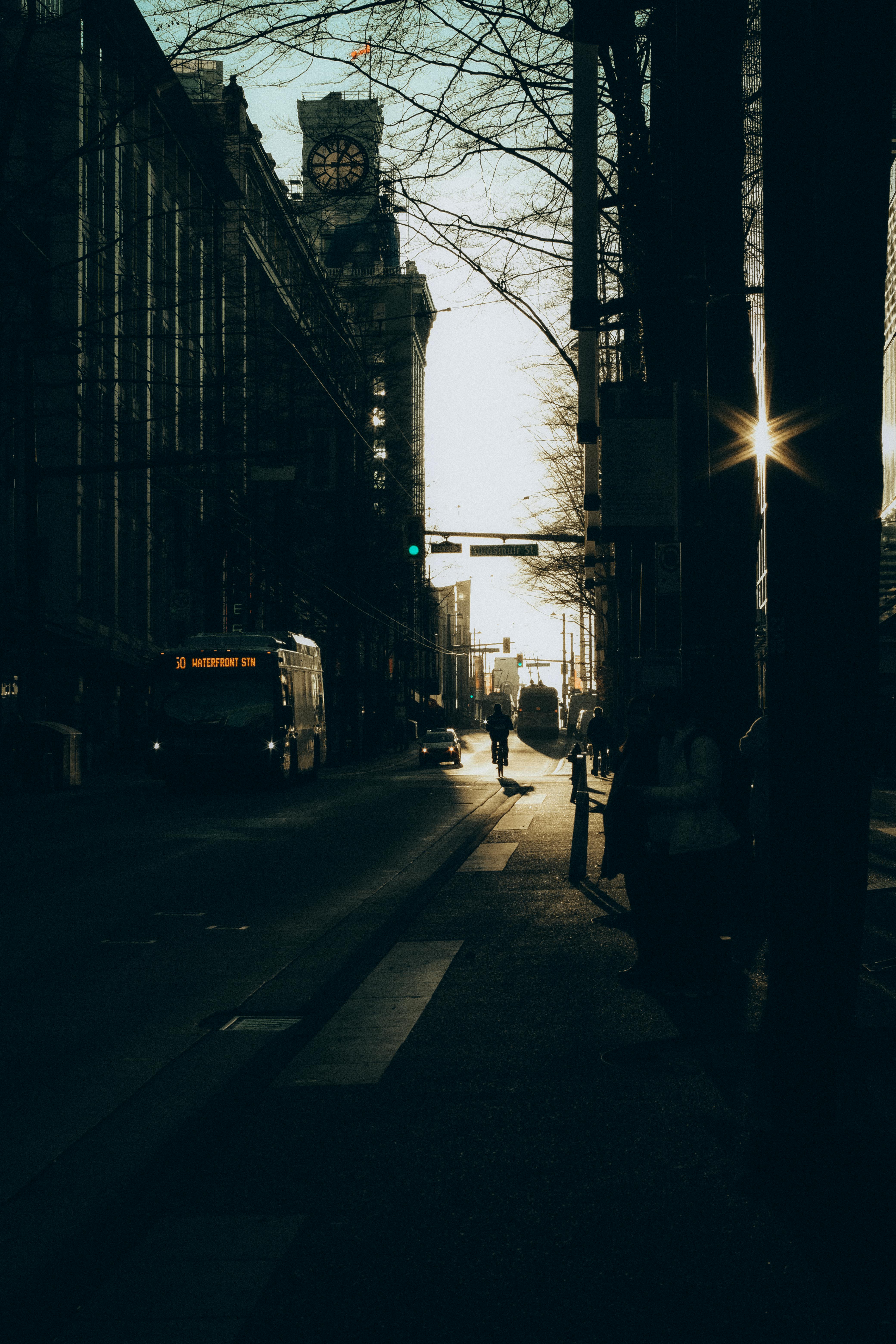 Silhouetted city street scene with a prominent clock tower at sunset, capturing urban life.