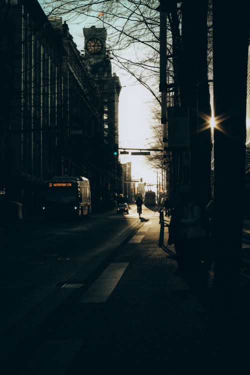 Free Silhouetted city street scene with a prominent clock tower at sunset, capturing urban life. Stock Photo