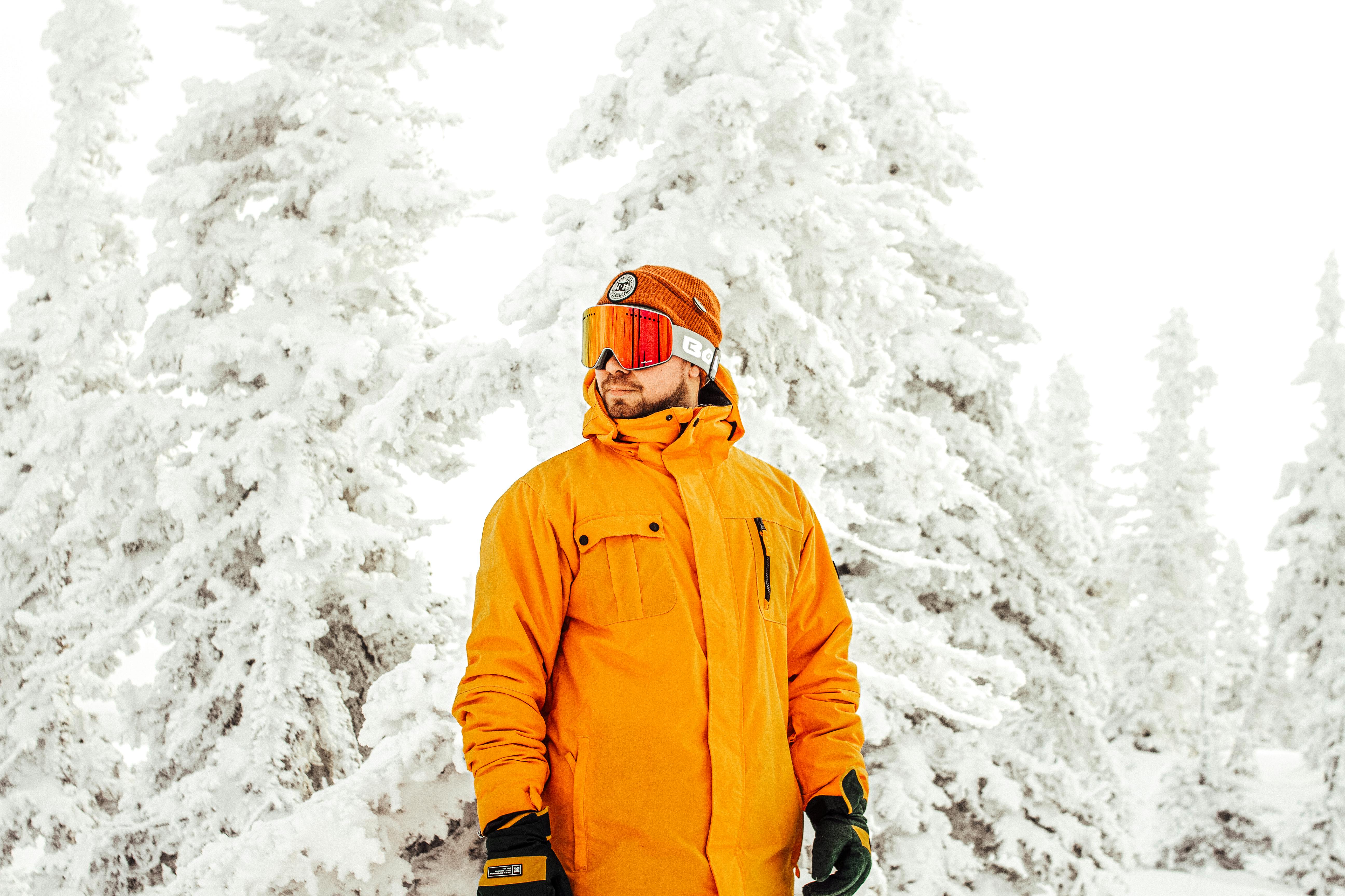 Man in bright snowboard gear stands amongst snow-covered trees, ready for winter adventure.
