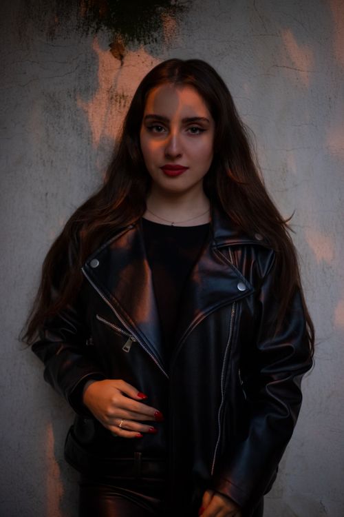 Free Stylish woman in leather jacket against textured wall with dramatic light and shadow. Stock Photo