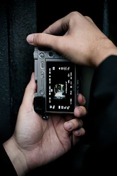 Hands holding a mirrorless camera capturing an urban scene, displaying settings.