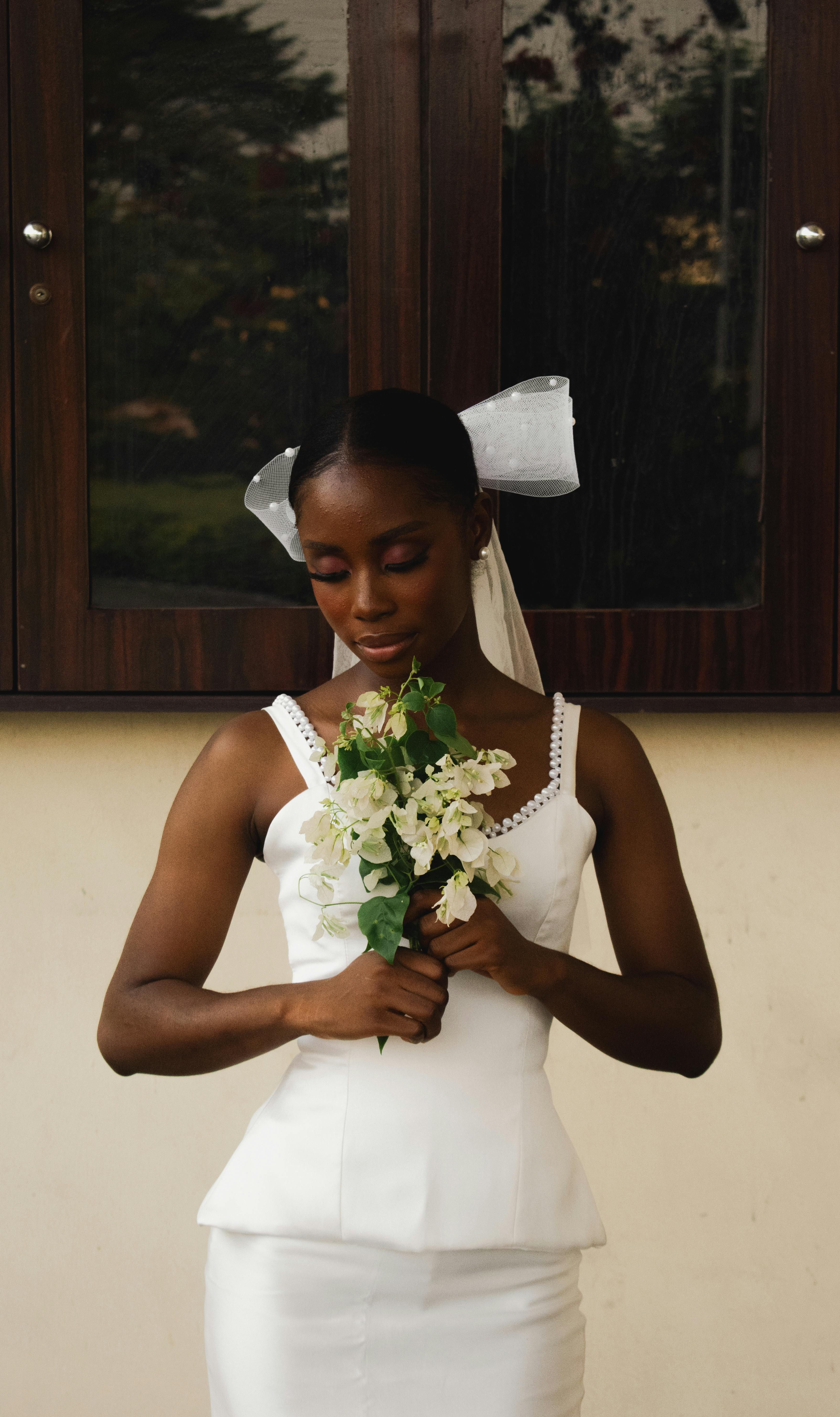 Bride in white dress holding bouquet in an outdoor setting, exuding vintage appeal.