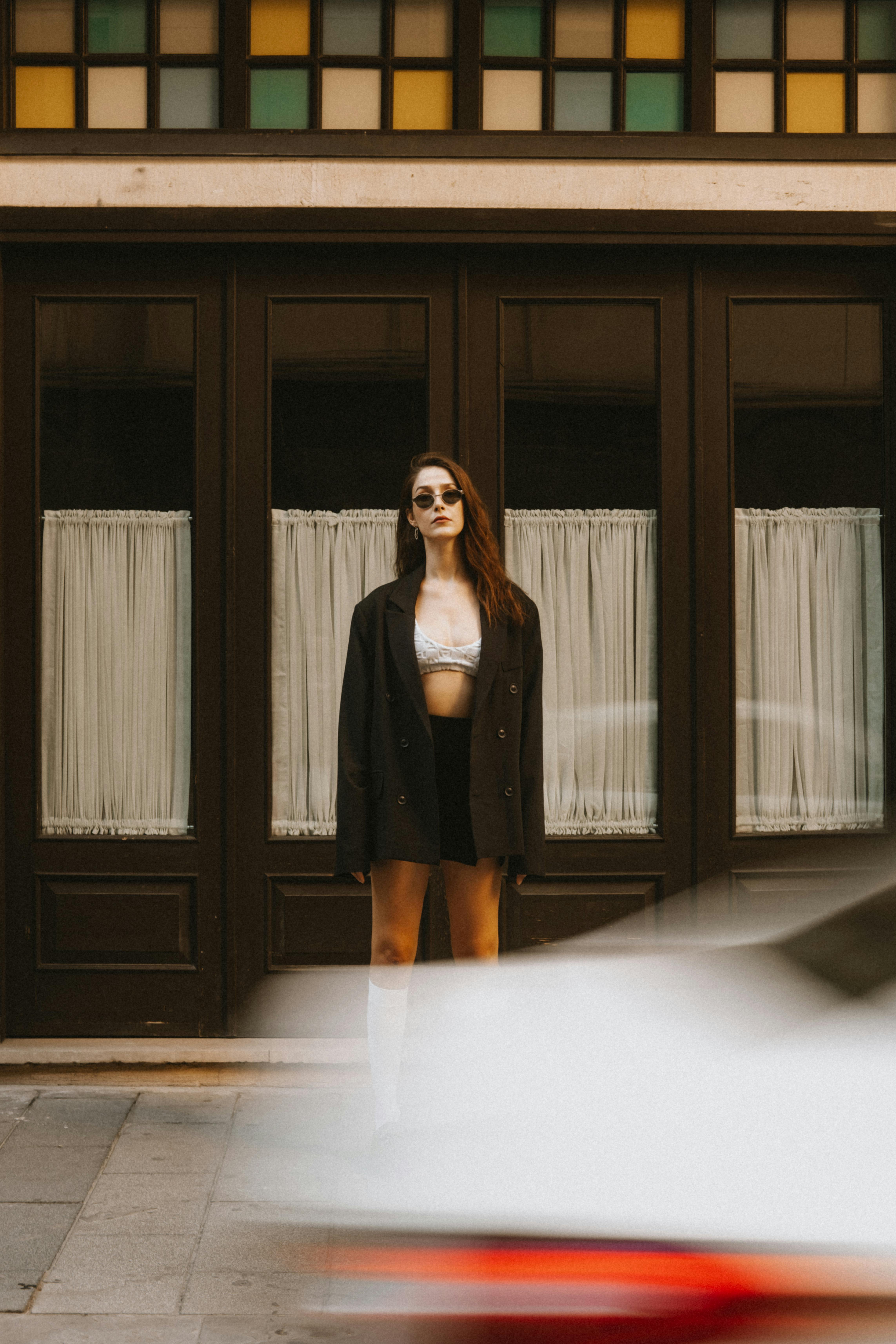 A fashionable woman posing confidently in front of a stylish urban backdrop with passing car motion blur.