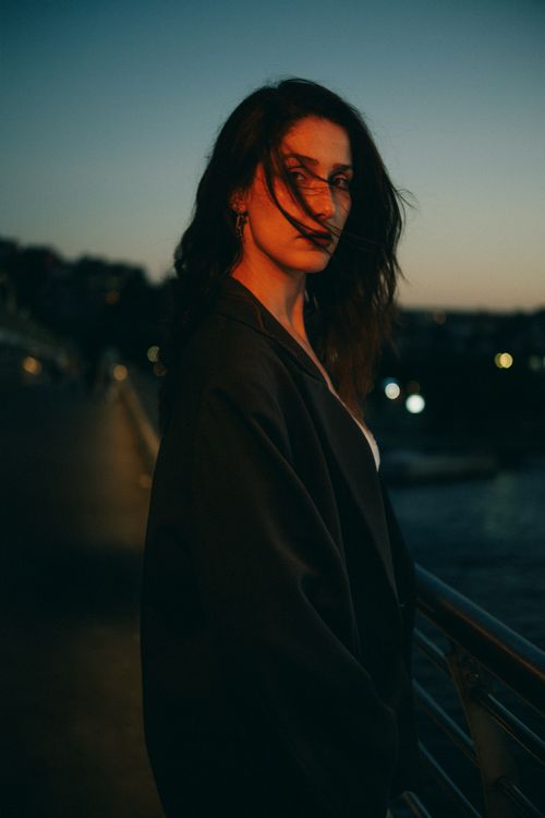 Free A contemplative woman standing on a bridge at twilight, calm and serene. Stock Photo